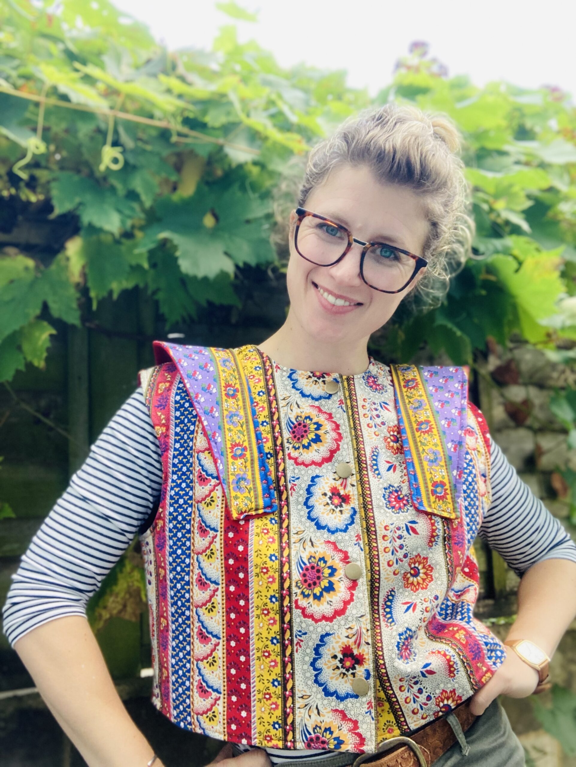 Woman with glasses smiling standing behind rail of handmade clothing